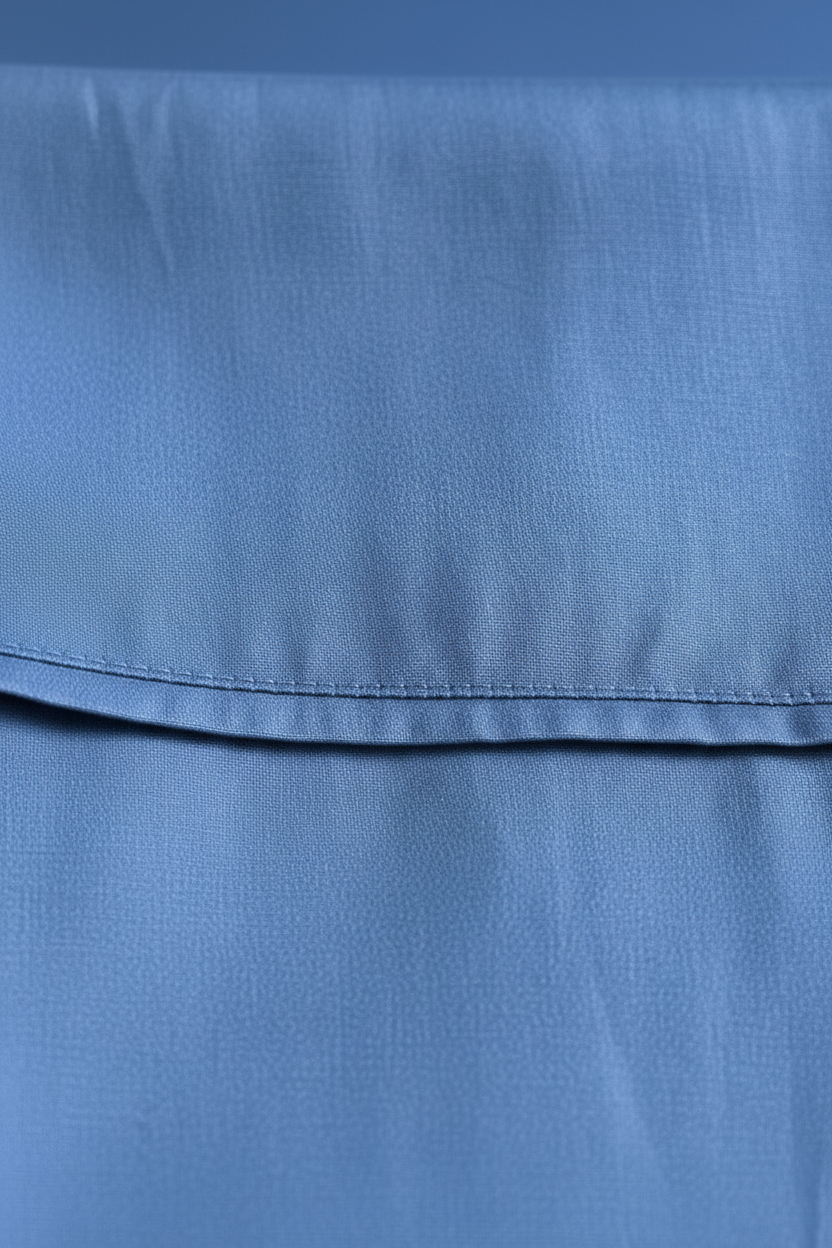 A close-up of a blue fabric surface with a horizontal stitched fold on flat sheet.