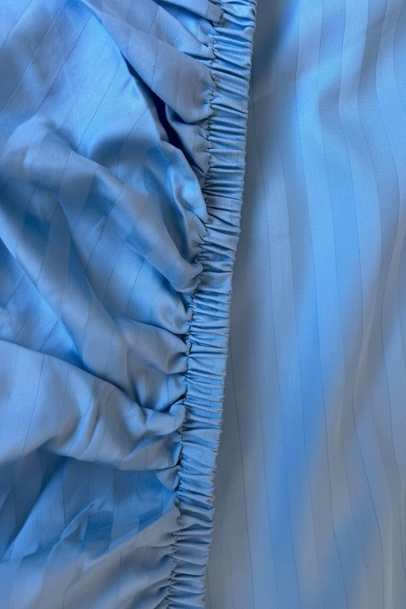 A close-up of a light blue striped fitted sheet sowing the 3/4 inch elastic width