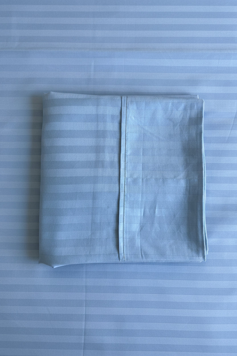 A folded light blue striped pillowcase  laid flat on a matching striped bedsheet.