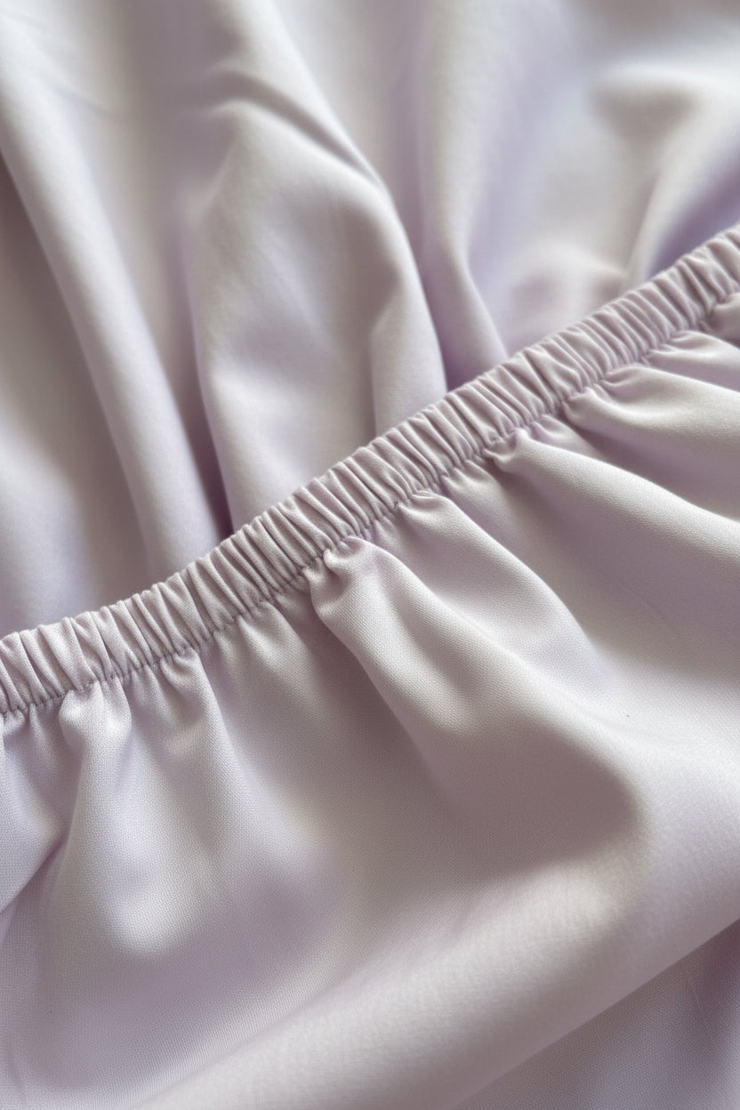 A close-up of a light lavender or pale lilac fabric with a gathered elastic waistband, showing the texture and folds of the material.